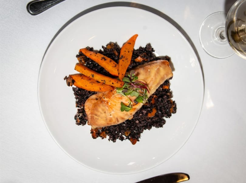 Salmon fillet with black rice, roasted carrots, and microgreens on a white plate.