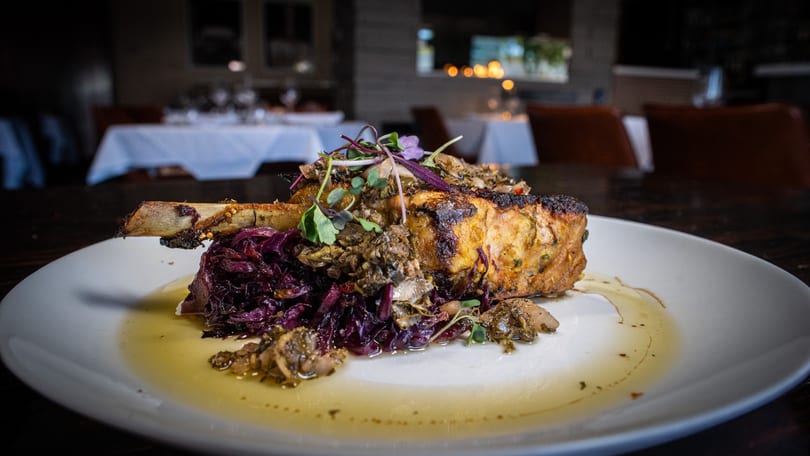 Pork chop with bone, red cabbage, and mushrooms on a white plate in a restaurant setting.