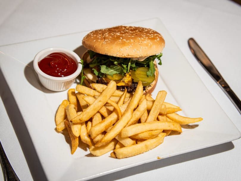 A gourmet burger with arugula, pickles, and cheese, served with golden fries and ketchup on a white plate.