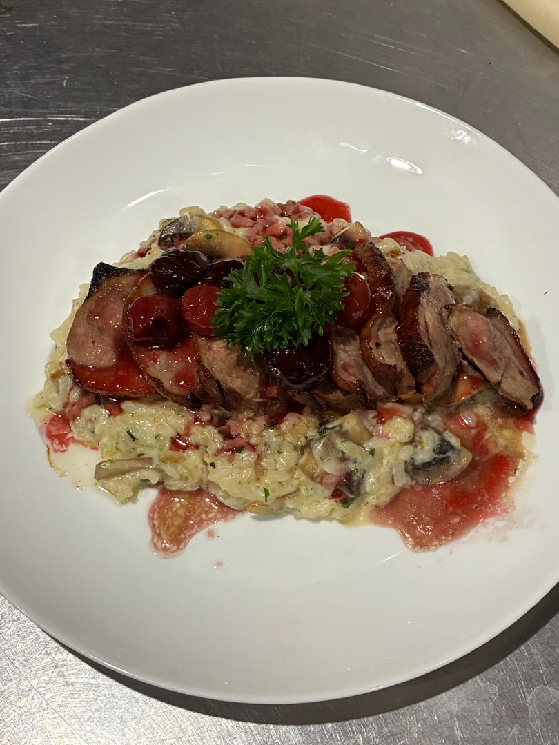 Sliced duck breast with cherry sauce and parsley on a bed of creamy risotto with mushrooms.